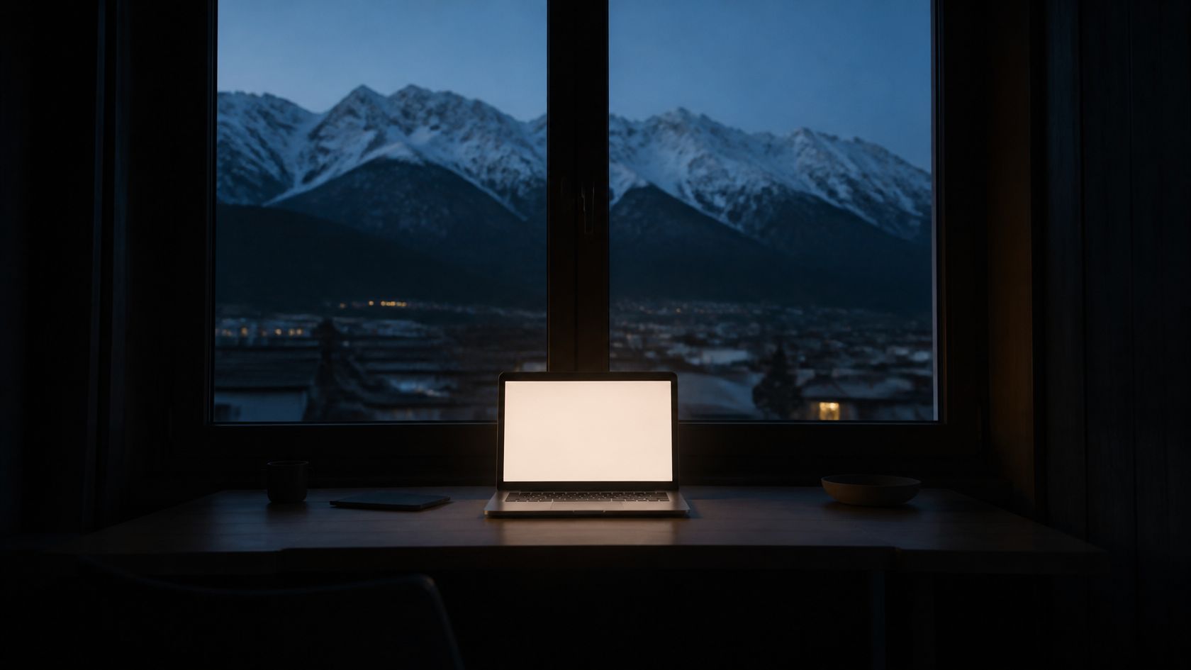 Arbeitsplatz am Fenster in der Abenddämmerung, dahinter die verschneite Nordkette über Innsbruck